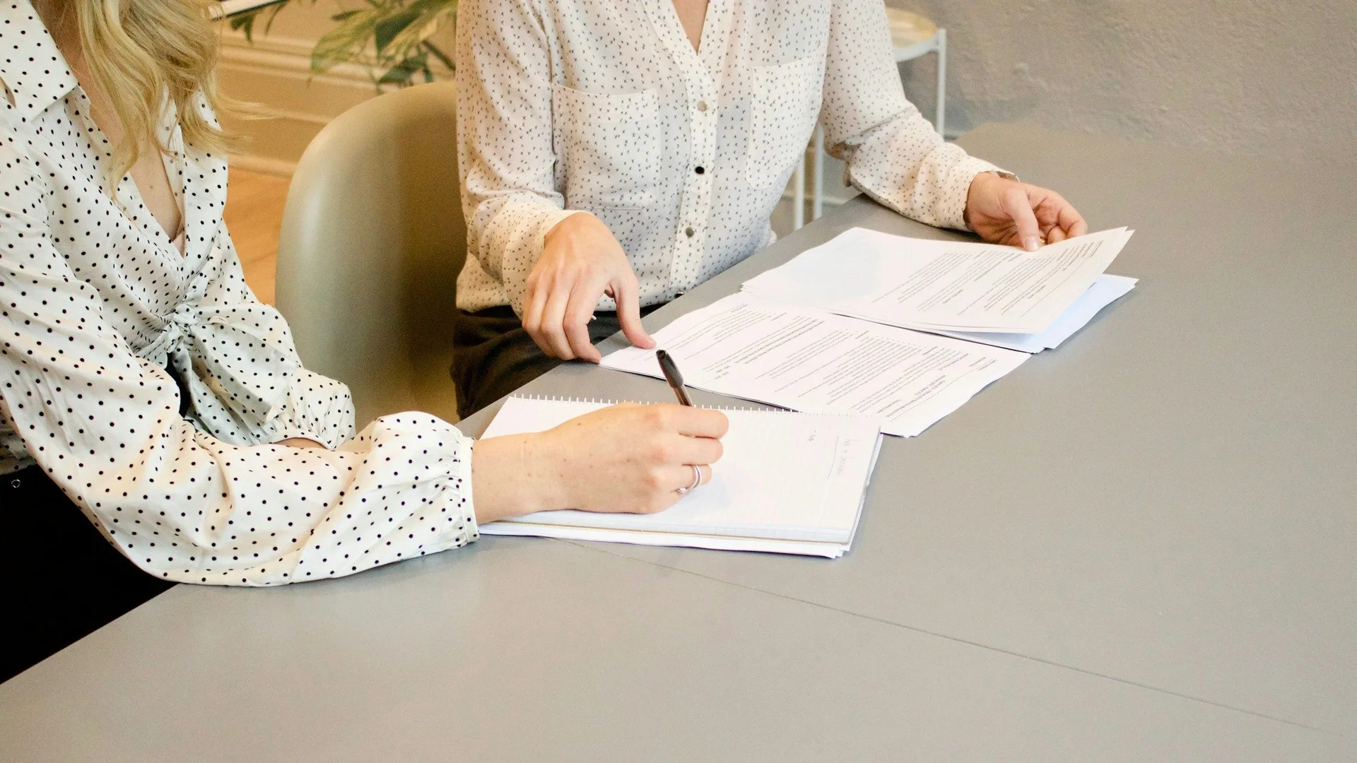 Vrouw ondertekent papieren aan tafel, tweede persoon kijkt mee